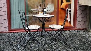 Eine Terrasse mit Tisch, zwei Stühlen, einer Weinflasche und einer Obstschale.