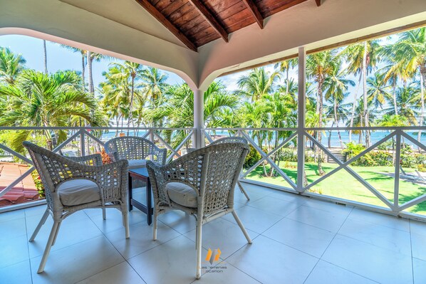 A covered outdoor area with wicker furniture and a view of palm trees and the ocean.
