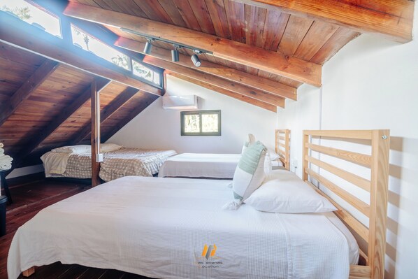 Un dormitorio acogedor en el ático con vigas de madera, una cama grande, dos camas más pequeñas y un tragaluz.