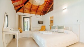 Een slaapkamer met een houten plafond, een bed met wit beddengoed, een nachtkastje, een stoel en een televisie.