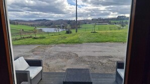 Vista de um alpendre com móveis de vime e uma área de cascalho que leva a um campo verde e um lago.