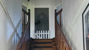 Uma escadaria de madeira com um cercado branco no topo, dando acesso a uma porta.