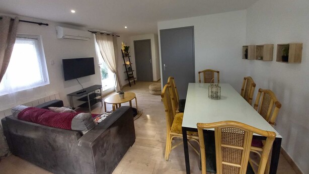 Una sala de estar con un sofá, un televisor, una mesa de comedor con sillas y una puerta que da a otra habitación.