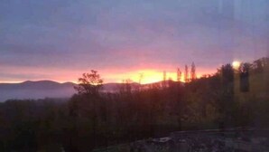 Un atardecer sobre un paisaje montañoso con una valla y árboles.