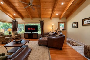 A spacious living room with a wooden ceiling, a large flat-screen TV, leather sofas, and a fireplace. - Riverside Cabin-River, Hot Tub, WIFI, Dogs OK (Leavenworth)