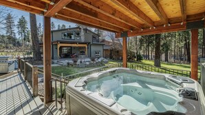 Een hottub op een houten terras met uitzicht op een tweelaags huis en een bebost gebied.