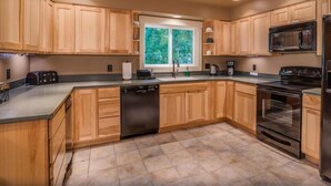 Una cocina moderna con armarios de madera, lavavajillas, microondas, estufa y ventana con vistas a zonas verdes.