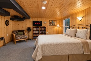 A cozy room with a bed, a bookshelf, a chair, and a wall-mounted TV displaying 'NETFLIX'. - Riverside Cabin-River, Hot Tub, WIFI, Dogs OK (Leavenworth)
