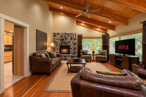 A cozy living room with a fireplace, leather sofas, a television, and a stone wall. - Riverside Cabin-River, Hot Tub, WIFI, Dogs OK (Leavenworth)