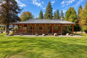 A lodge with a covered porch, a stone fireplace, and a view of the surrounding forest. - Riverside Cabin-River, Hot Tub, WIFI, Dogs OK (Leavenworth)