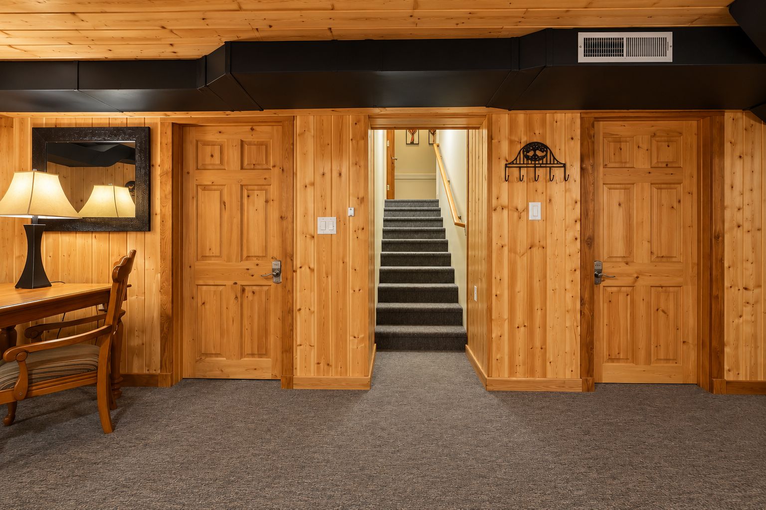 A room with a wooden floor, a desk with a lamp, and a staircase leading to another level.