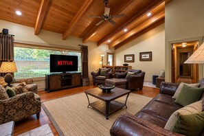 A living room with a television, leather sofas, a coffee table, and a ceiling fan.