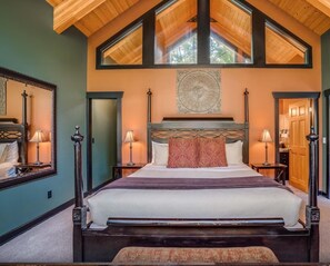 A bedroom with a large bed, wooden ceiling beams, and a skylight.