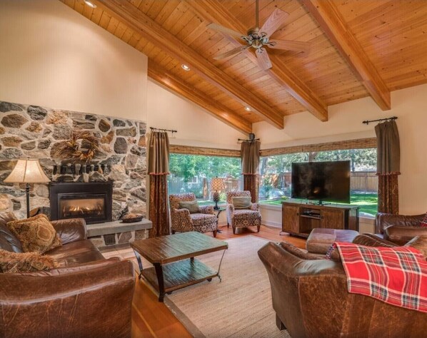 A cozy living room with a stone fireplace, leather sofas, a television, and a ceiling fan.