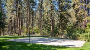 A well-maintained golf course with a sand bunker, surrounded by tall pine trees.