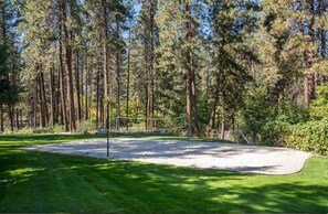A well-maintained golf course with a sand bunker, surrounded by tall pine trees.