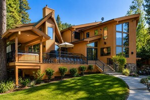 A modern wooden house with a deck, outdoor seating, and a stone wall.