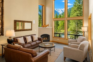 A living room with a fireplace, leather sofas, a coffee table, and large windows with a mountain view.