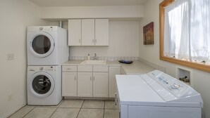 A laundry room with two stacked washing machines, a sink, and a window with curtains.