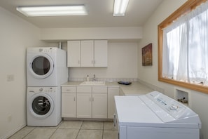 A laundry room with two stacked washing machines, a sink, and a window with curtains.