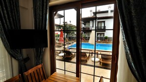 Una habitación con vista a una piscina al aire libre, un balcón con barandilla y un televisor montado en la pared.