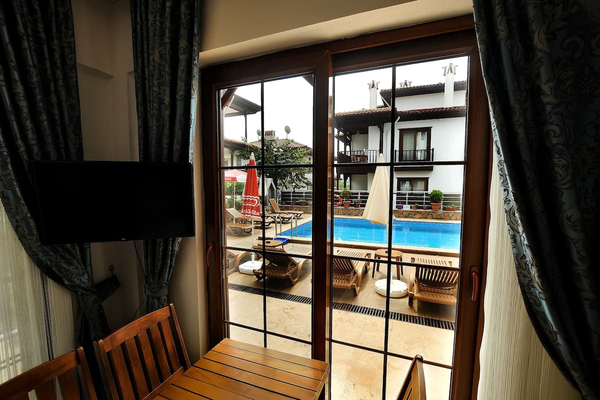 A room with a view of an outdoor swimming pool, a balcony with a railing, and a television mounted on the wall.