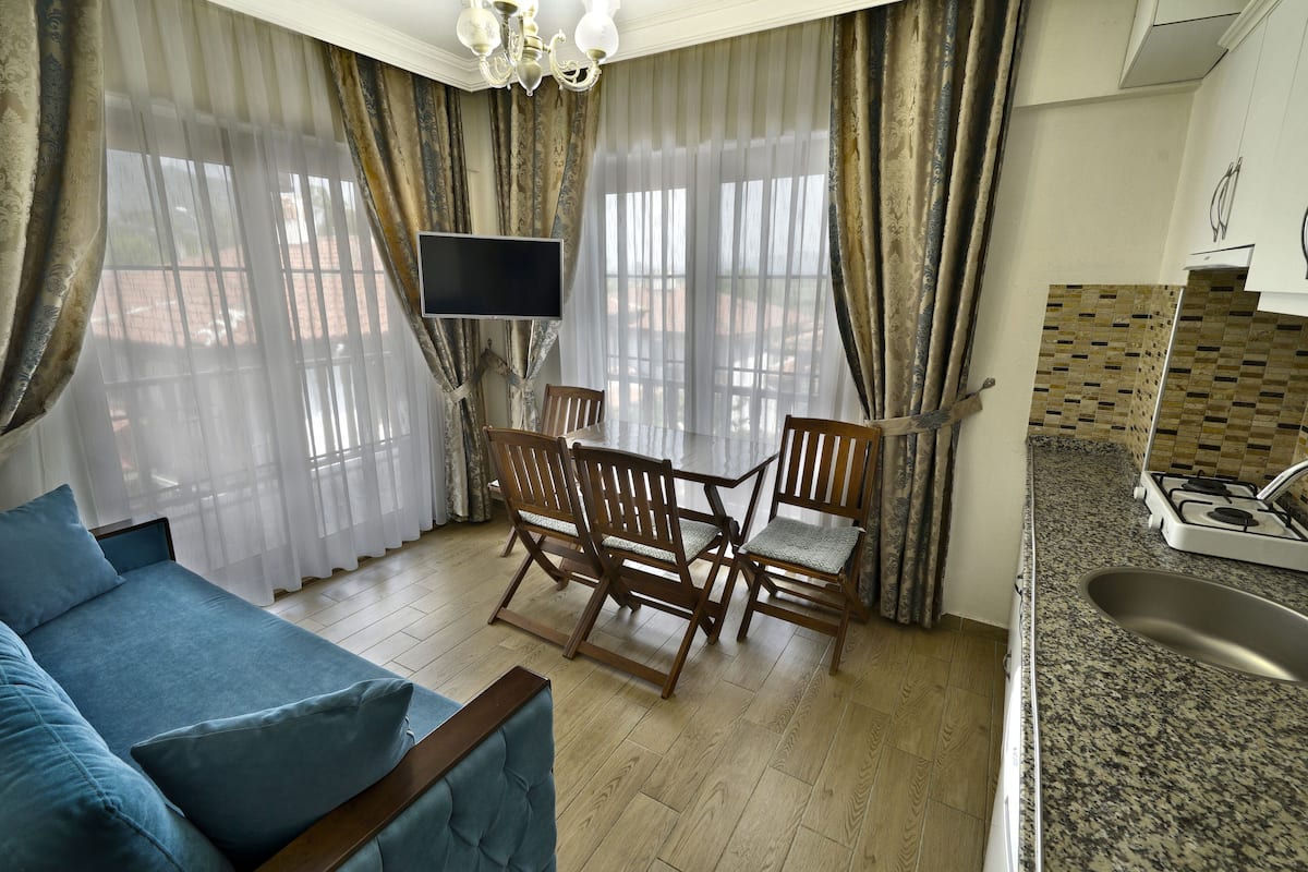 A living room with a sofa, a TV, wooden chairs, and a kitchen area with a sink and stove.