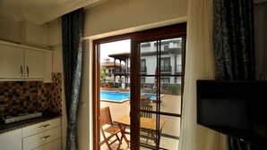 Habitación con cocina, comedor con mesa y sillas, televisor y puerta corrediza de vidrio que da a un área de piscina al aire libre.