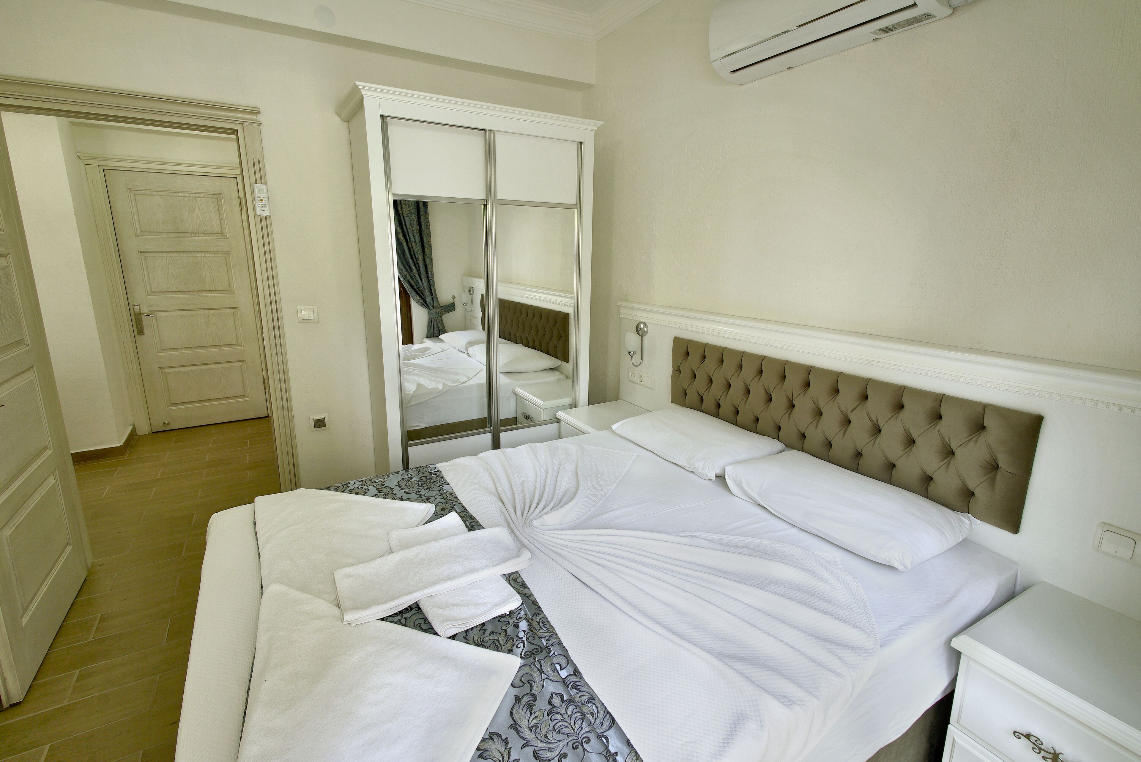 A neatly made bed with white linens, a tufted headboard, and a bedside table with a drawer.