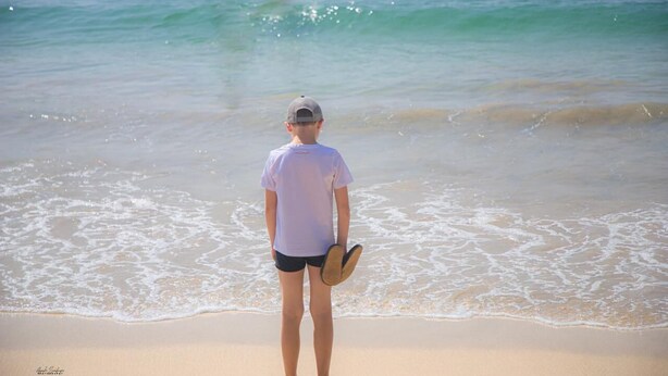 Una persona in piedi su una spiaggia sabbiosa, con un paddleboard, che guarda l'oceano.