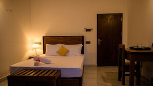 Un letto rifatto con cura, una testiera in legno, un comodino con una lampada e un tavolo da pranzo con sedie in una camera d'albergo.