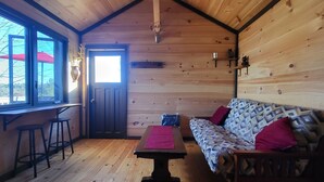 L’intérieur d’un chalet accueillant, avec un plafond en bois, une table à manger entourée de tabourets, un canapé et une fenêtre donnant sur l’extérieur, où se trouve un parasol rouge.