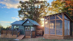 Une petite cabane dotée d’une terrasse et d’un grand porche grillagé.