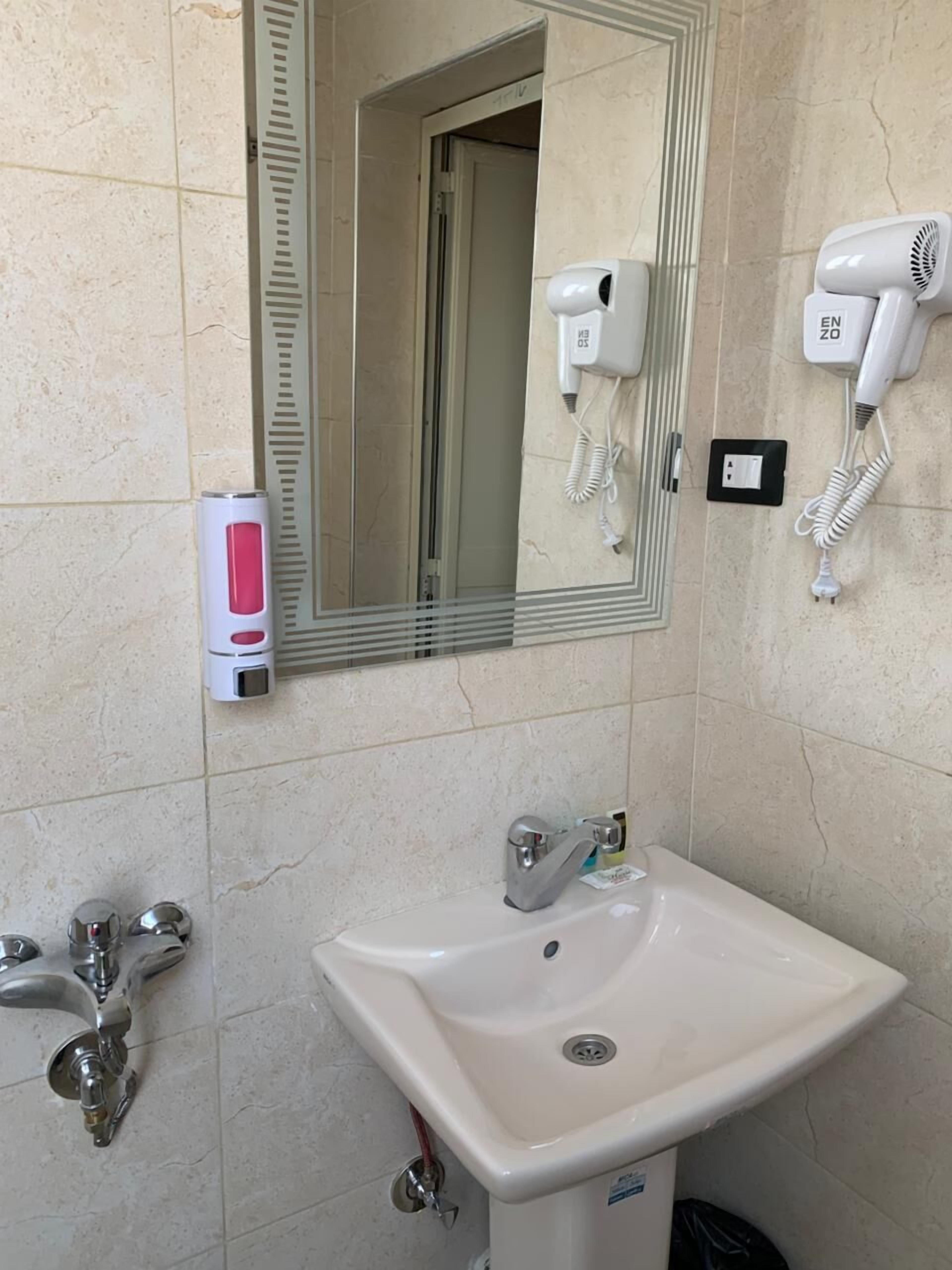 A bathroom with a sink, mirror, and two hair dryers mounted on the wall.