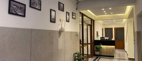 A hotel reception area with a reception desk, framed pictures on the wall, a reception sign, and a potted plant.