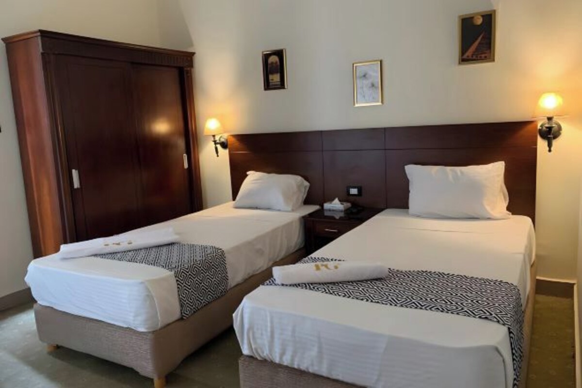Habitación de hotel con dos camas individuales, un armario y una mesita de noche con lámpara.
