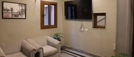 Een woonkamer met een bank, een salontafel, een aan de muur bevestigde televisie en een potplant.