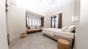 Quarto com cama, assento à janela, ventilador de teto e uma grande janela com cortinas.