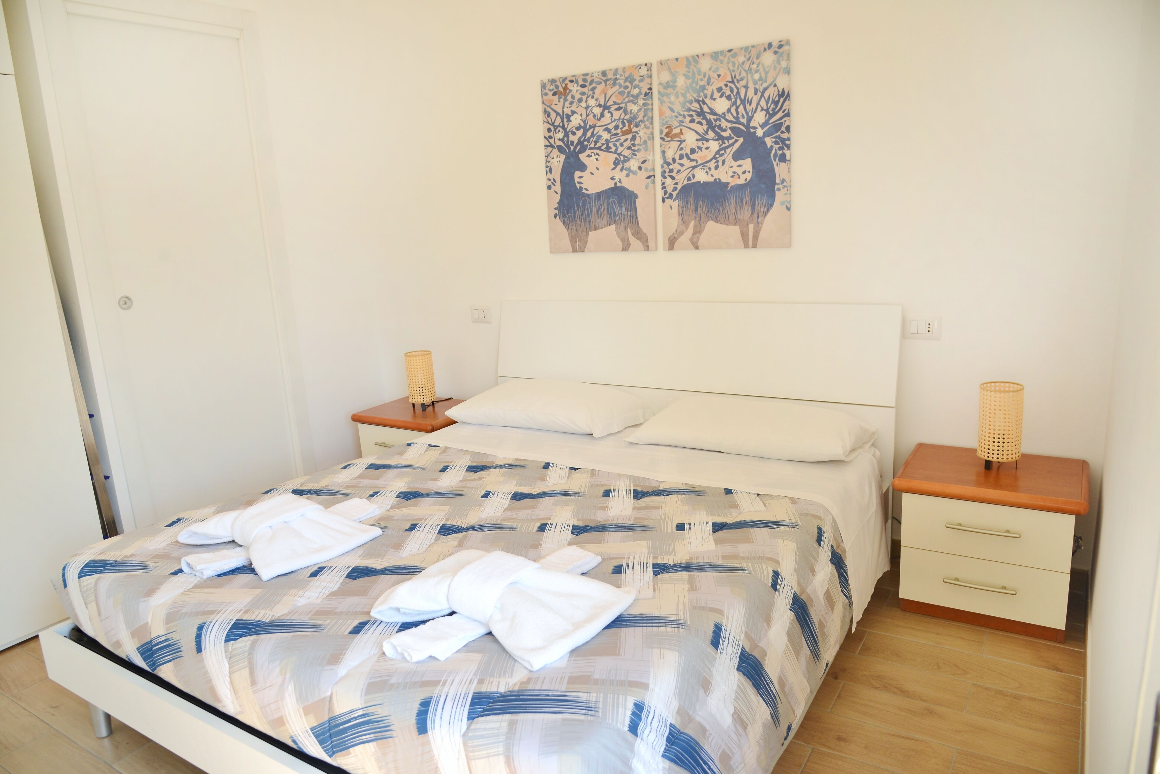 A neatly made bed with a patterned bedspread, two bedside tables with lamps, and a wall art piece above the bed.