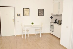 A small, clean room with a white door, a dining table with two chairs, a small potted plant, and a kitchenette with a stove and oven. - Bogliasco Home (Aurelio) (Roma)