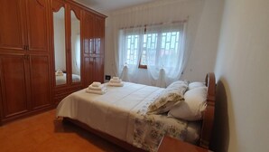 A bedroom with a large wooden wardrobe, a bed with white linens, and a window with sheer curtains. - Room in B&B - Comfortable Room With Spacious Kitchen - Suite Colosseo (Rome)