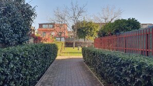 A paved pathway flanked by neatly trimmed hedges, leading to a building with a red facade. - Room in B&B - Comfortable Room With Spacious Kitchen - Suite Colosseo (Rome)