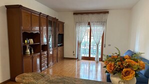 A spacious living room with a wooden cabinet, a television, and a vase with flowers on a granite countertop. - Room in B&B - Comfortable Room With Spacious Kitchen - Suite Colosseo (Rome)
