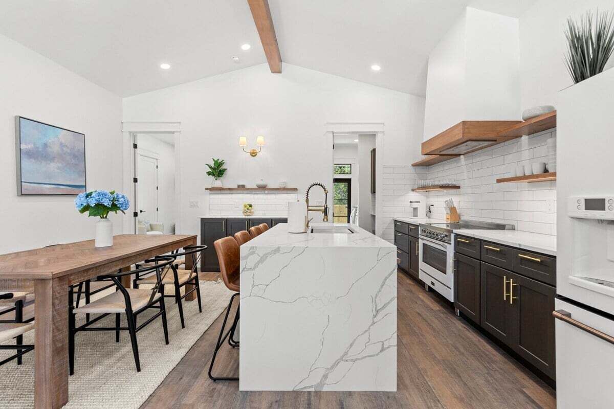 Une cuisine moderne dotée d ’un îlot en marbre, de meubles de couleur sombre et d’éléments décoratifs en bois.