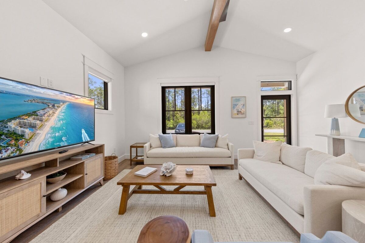 Amplia sala de estar con un televisor de pantalla plana grande, un sofá color beige, una mesa de centro de madera y vista al océano a través de amplias ventanas.
