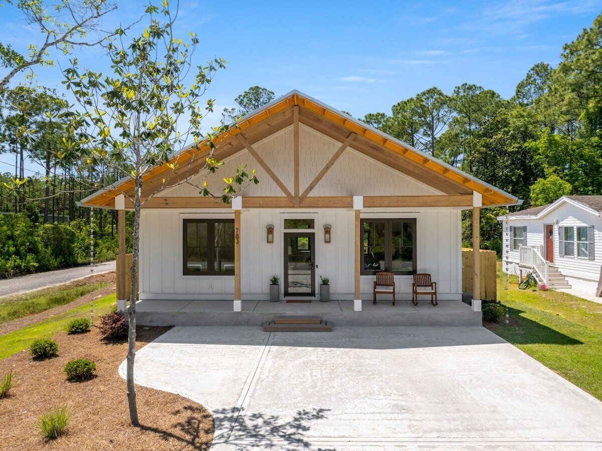 A single-story building with a gabled roof, a covered porch with two chairs, and a small attached garage.