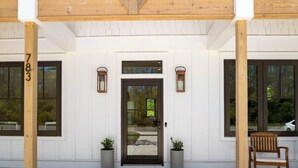A building entrance with a wooden door, two potted plants, a bench, and a number '783' on a post.