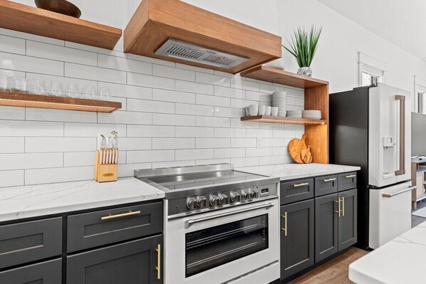 A modern kitchen with white subway tiles, a stainless steel range, and black cabinets with gold handles. - Luxury Home, Fenced Yard, Pine & Pear, Hot Tub, Deck Near Bay, Fire Pit, Grill (Santa Rosa Beach)
