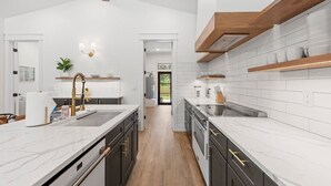 A modern kitchen with white marble countertops, dark cabinetry, and wooden beams.