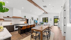 A modern kitchen with a wooden dining table, bar stools, and a large plant.